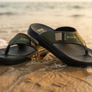Men's olive green and black outdoor flip flop slippers with cushioned footbed, soft toe-post strap, anti-slip sole, displayed on a sandy beach for casual summer wear.